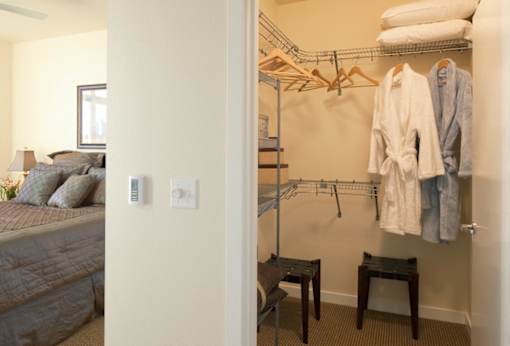 A bedroom with a bed, nightstand, and a closet with clothes.