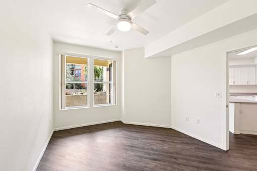 A room with a ceiling fan and a window showing a view of a building.