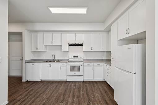 A white kitchen with wooden floors and white appliances.