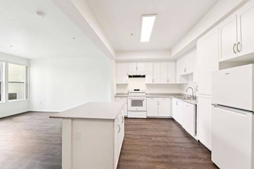A white kitchen with wood floors and white appliances.
