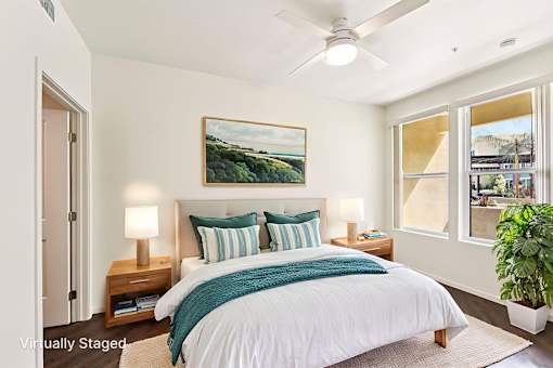 A bedroom with a bed, pillows, a ceiling fan, and a painting on the wall.