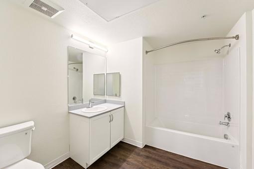 A white bathroom with a sink, mirror, and bathtub.