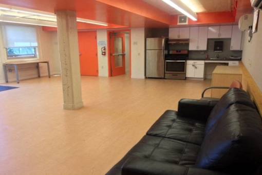 A black leather couch sits in a room with orange walls and a kitchen area in the background.