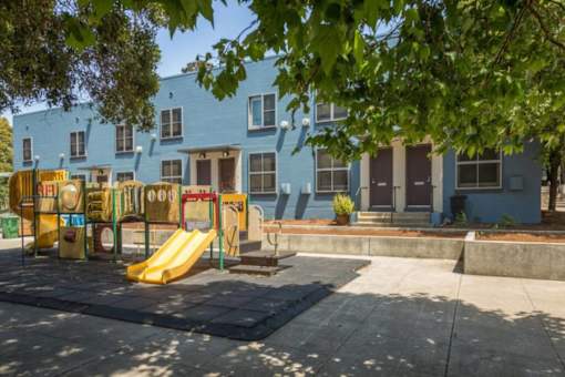 A playground with a yellow slide in front of a blue building.