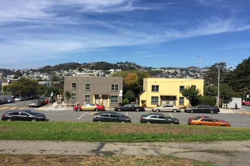 A parking lot with cars and two buildings in the background.