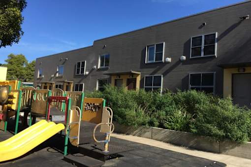 A playground with a yellow slide in front of a grey building.