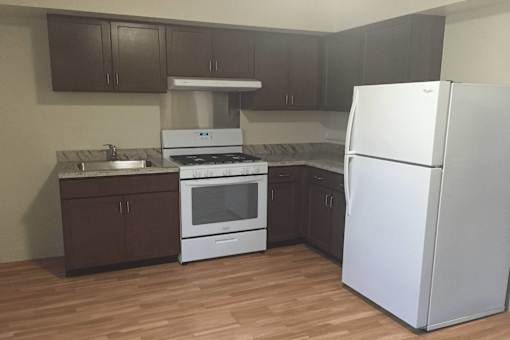 A white refrigerator stands in a kitchen with brown cabinets and a white stove.