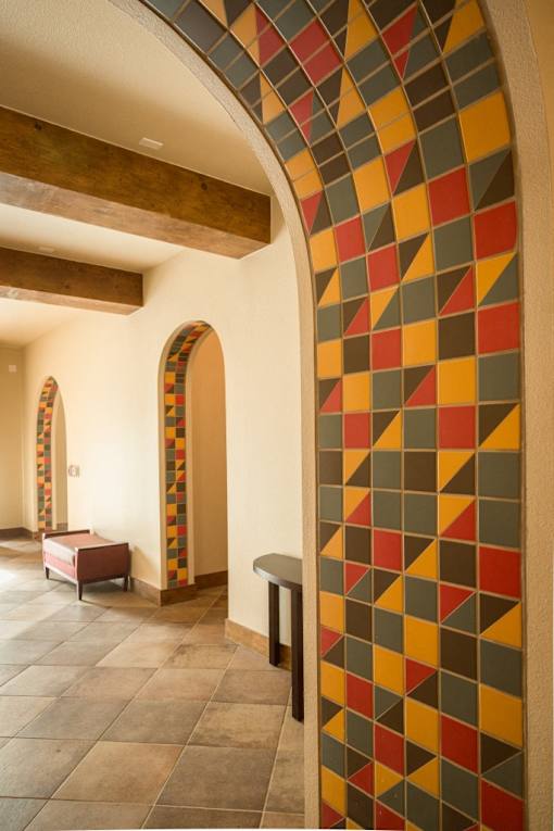 A hallway with a colorful mosaic wall and arched doorways.
