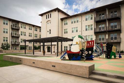 A playground area with a slide and a teddy bear slide in front of a building.