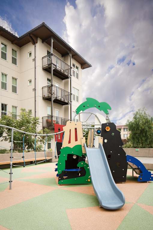 A playground with a slide and a green dinosaur.