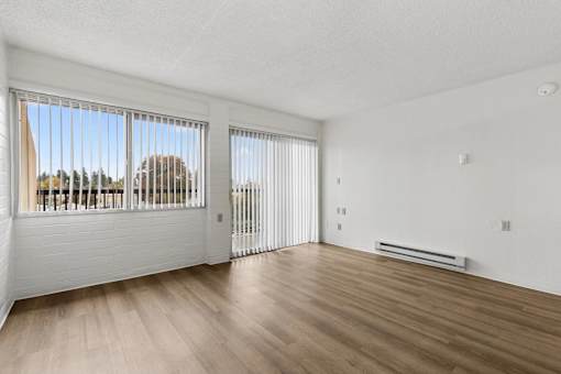 A room with wooden floors and white walls, with a view of trees outside the window.
