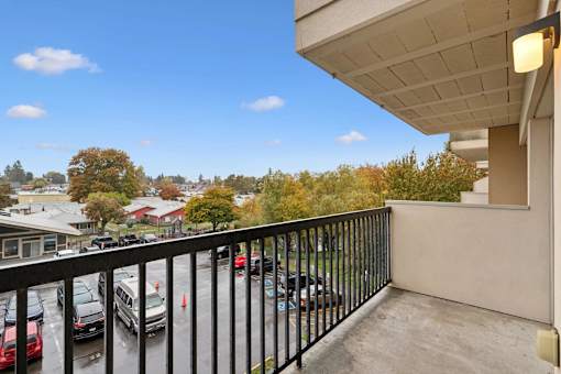 A balcony with a black railing overlooks a parking lot and trees.