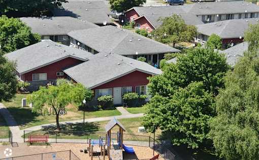 A playground area with a slide and a swing set in front of a red building.