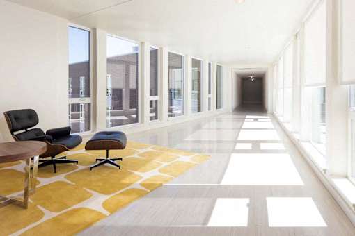 A long hallway with a yellow and white carpet and black chairs.