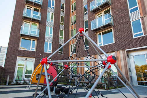 A playground structure with red and yellow elements in front of a brick building.