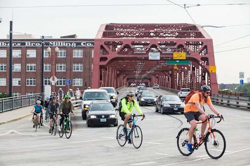A group of cyclists are riding on a bridge with a brick building in the background.