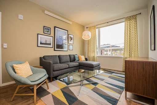 A living room with a grey couch, a yellow pillow, a glass coffee table and a yellow chair.
