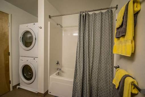 A bathroom with a white tub, a shower curtain, a yellow towel, and a white washing machine.