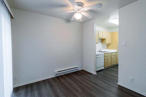 A room with a ceiling fan and a kitchen in the background.