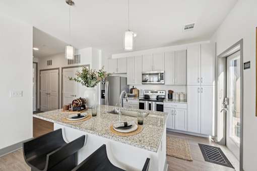 A modern kitchen with a granite countertop and black chairs.