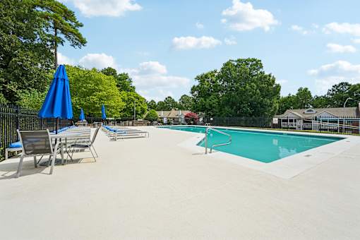 A pool with a blue umbrella and chairs.