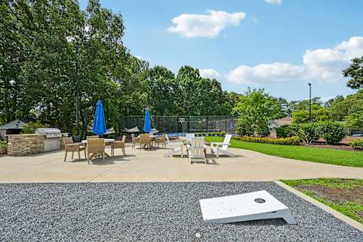 A concrete patio with chairs and umbrellas surrounded by greenery.