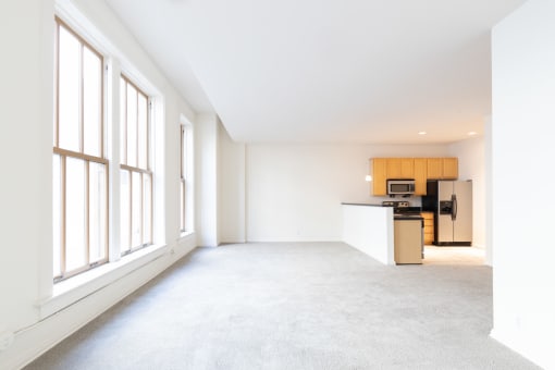 an empty living room with large windows and a kitchen in the background at 26 West, Managed by Buckingham Urban Living, Indianapolis