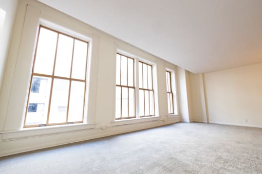 an empty living room with three large windows at 26 West, Managed by Buckingham Urban Living, Indianapolis