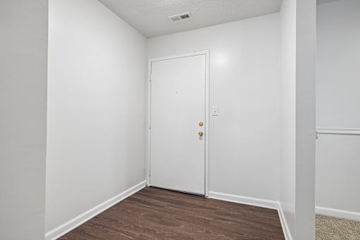 A white door with a gold handle is in a room with white walls and a wooden floor.