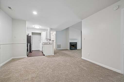 A spacious living room with a fireplace and a kitchen area in the background.