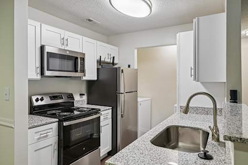 A kitchen with a black refrigerator, white cabinets, and a granite countertop.