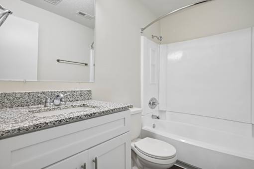 A white bathroom with a granite countertop and a white bathtub.