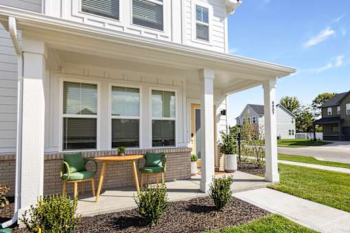 A white house with a porch and green chairs.