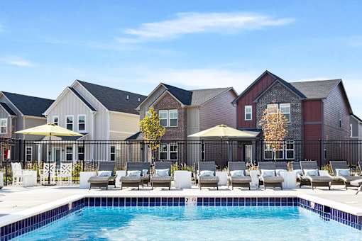 A pool area with lounge chairs and umbrellas in front of a row of houses.