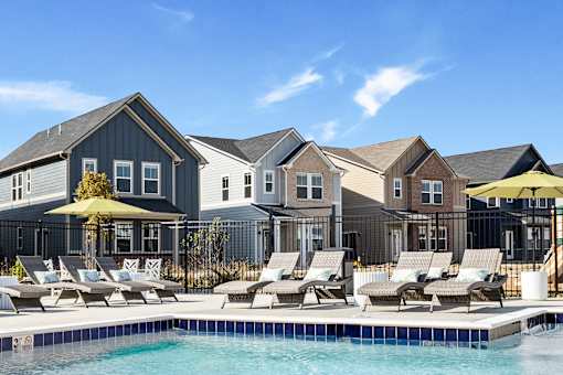 A pool with lounge chairs and umbrellas in front of a row of houses.