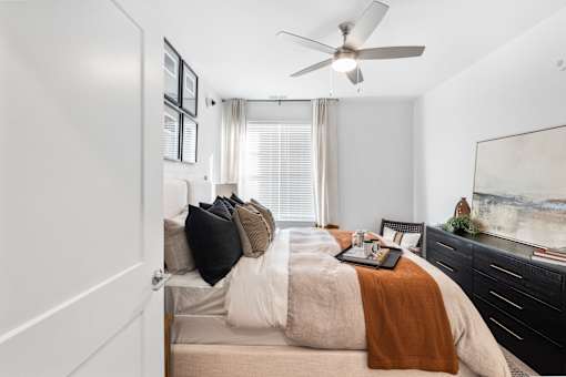 A bedroom with a bed, a ceiling fan, and a painting on the wall.