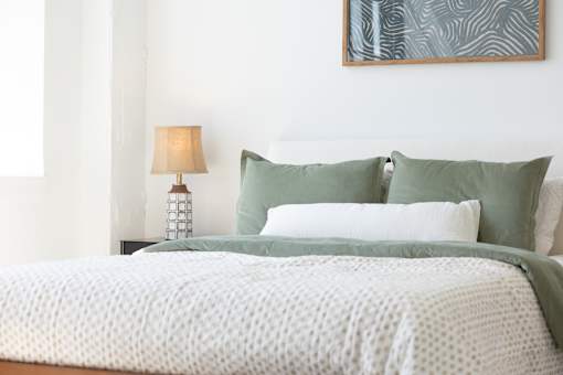Bedroom bedding detail with green linens and a bedside lamp