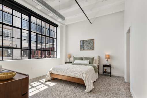 Bedroom with walnut bed frame and a wall of steel factory windows at Cole Motor in Indianapolis