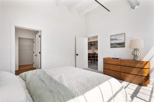 Bedroom with walk-in closet, dresser and a sightline through to the kitchen