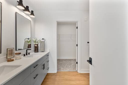 Bathroom double vanity with sconces and a walk-in closet beyond