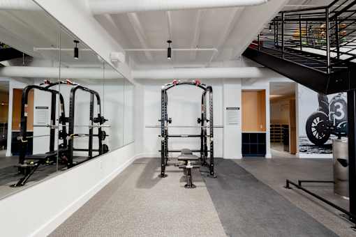 Squat rack and weight bench in the Cole Motor Apartments fitness center in Indianapolis, featuring mirrored walls and exposed industrial ceilings.
