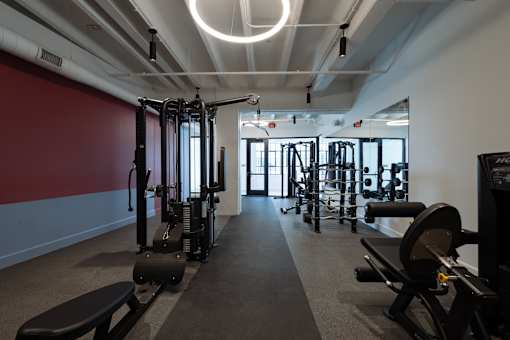 Strength training section of the Cole Motor Apartments fitness center in Indianapolis featuring cable machines, weight equipment, mirrors, and rubber flooring.