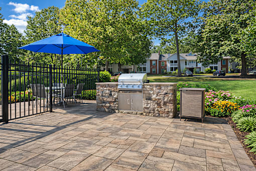 A blue umbrella is on a patio with a stone wall and a mailbox.