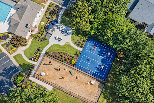 A tennis court surrounded by trees and a playground.
