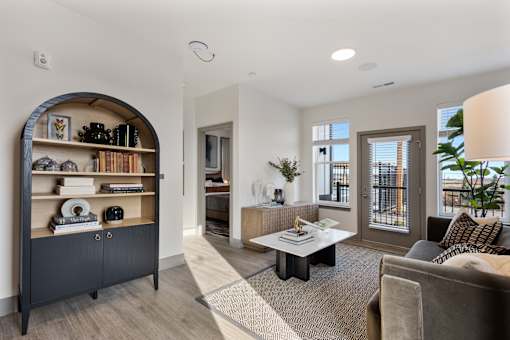 Model apartment living room at Montage West Lafayette featuring an open layout, modern furnishings, decorative shelving, and large windows with natural light.