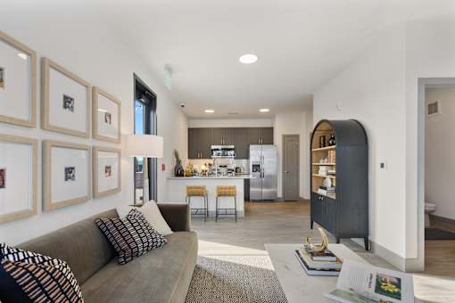 Model apartment living room with modern sofa, curated wall art, open kitchen with island seating, stainless steel appliances, and contemporary finishes at Montage
