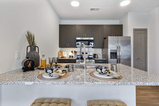 Model apartment kitchen at Montage West Lafayette featuring granite countertops, stainless steel appliances, modern cabinetry, and a large kitchen island with seating.