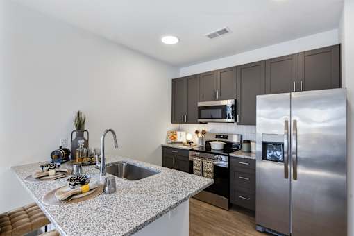 Modern apartment kitchen with granite island, stainless steel appliances, dark cabinetry, and undermount sink at Montage apartment community