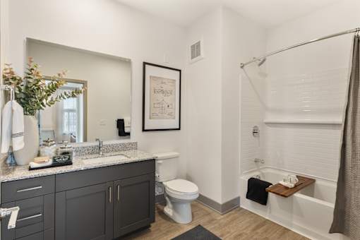 Model apartment bathroom at Montage West Lafayette featuring granite countertops, modern vanity cabinetry, framed mirror, and contemporary finishes.