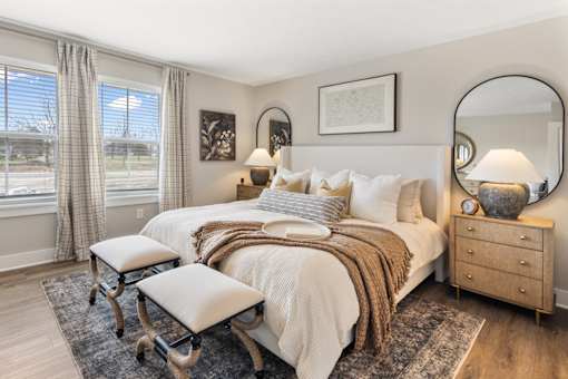 Spacious primary bedroom in single-family rental home at Mural Lewis Center featuring large windows, plush bedding, neutral tones, wall art, and soft carpeting